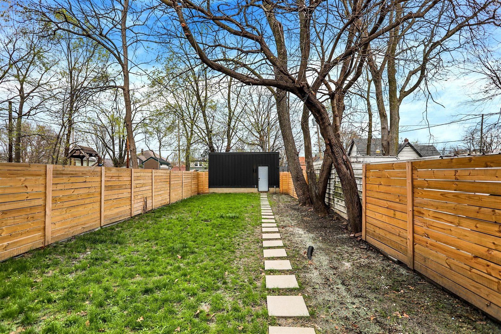 Fully fenced backyard with paver walkway, mature tree, and matching black storage shed