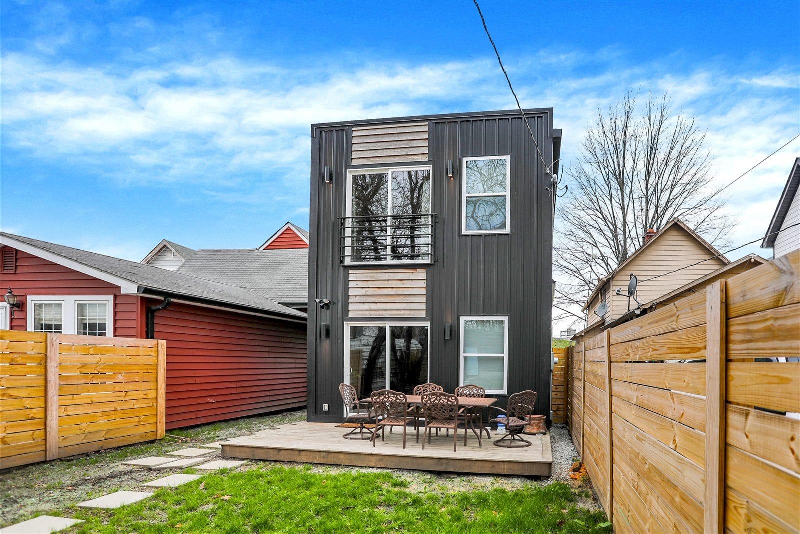 Rear exterior in black board-and-batten with cedar-accent Juliet balcony and dining deck