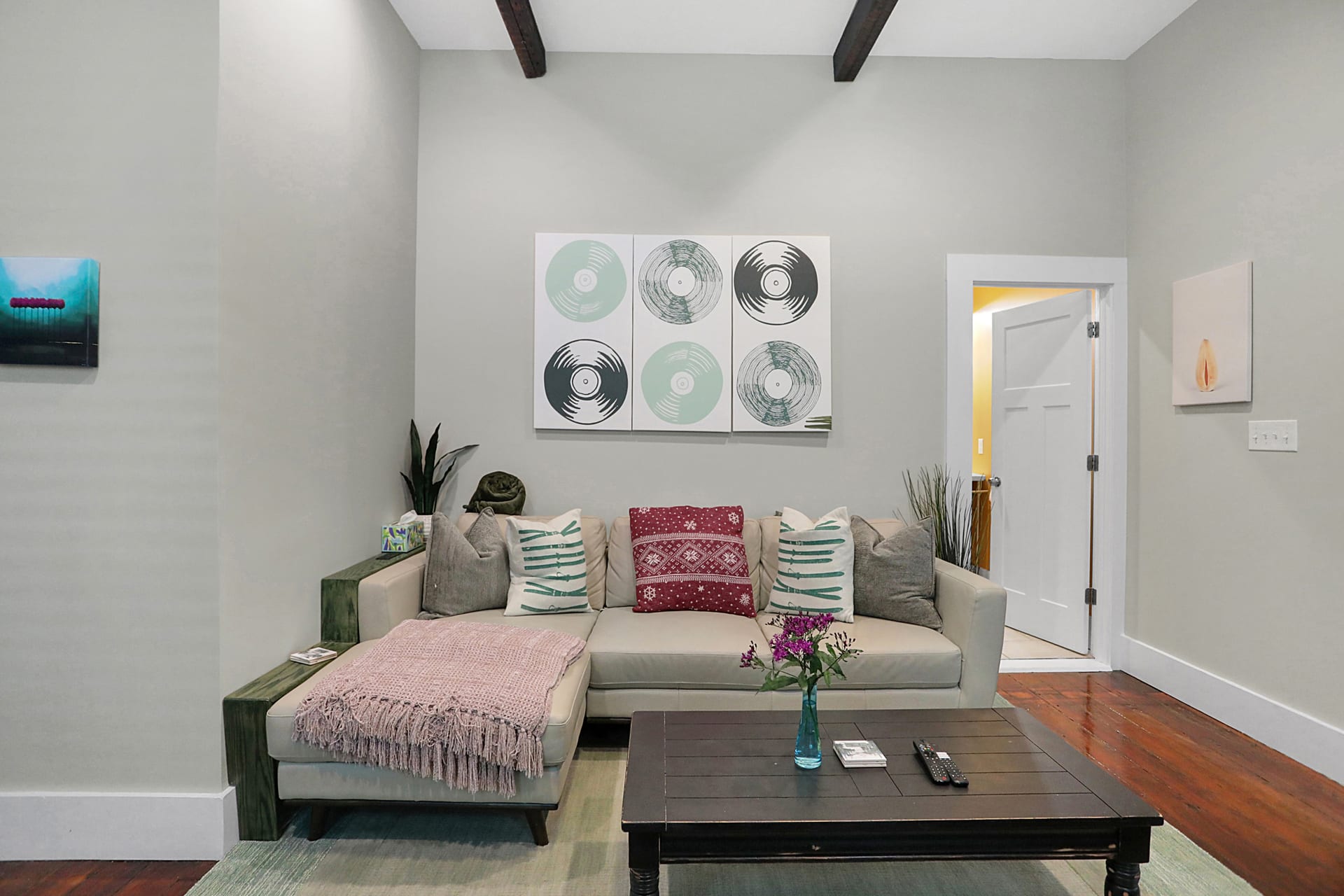 Sectional sofa under a triptych of vinyl-record art, with soaring ceilings and dark wood beams overhead