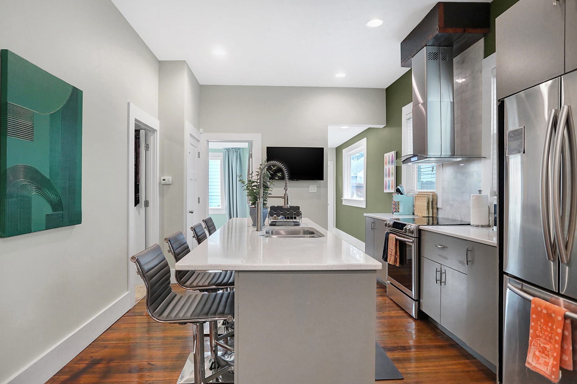 Kitchen quartz island with seating for four, stainless appliances, and the green accent wall facing the living room
