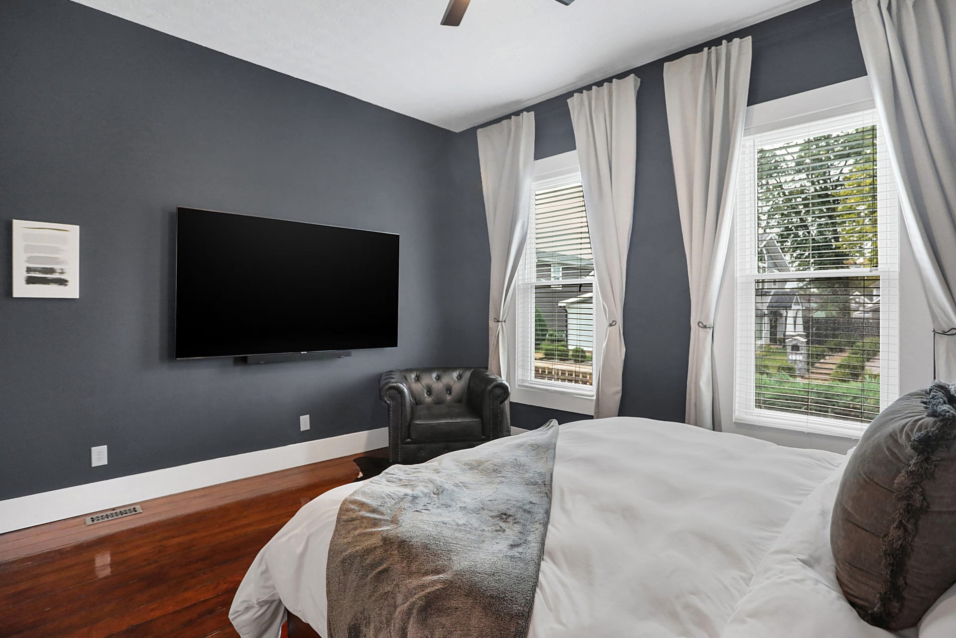 Primary bedroom with wall-mounted flat-screen TV, leather accent chair, and views to the backyard