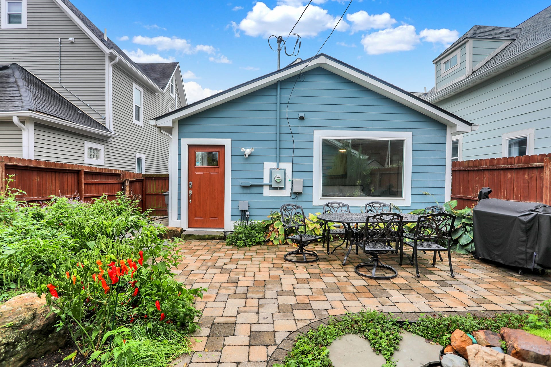 Rear of the blue cottage showing the large living-room window, patio, grill, and side entry door